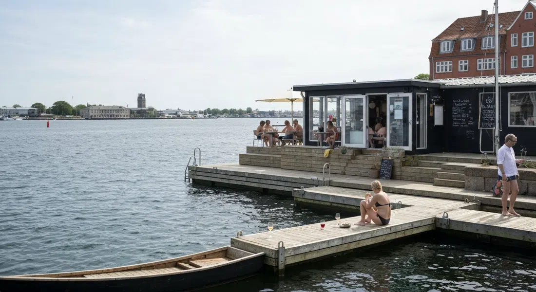 La Barchinas kleine Bootshaus-Terrasse und Schwimmsteg am Hafenrand, mit ein paar Gästen in Badekleidung und Gläsern mit Natural Wine